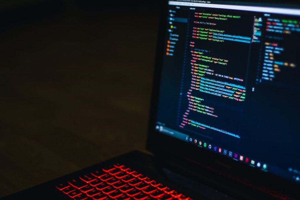 A laptop with a red-backlit keyboard displays coding software on its screen, showcasing HTML and CSS with colored syntax against a dark background. The image is captured in a dimly lit environment, highlighting the importance of electronic recycling in Atlanta, GA for sustainable tech use.