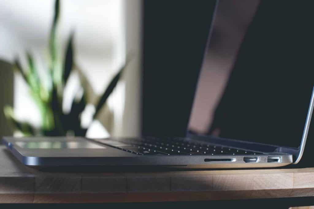 A sleek, silver laptop on a wooden surface, partially open with its screen dark. In the background, a blurred houseplant basks in natural light. Consider electronic recycling in Atlanta GA to ensure this beauty finds new life when its time is up, contributing to a greener future.
