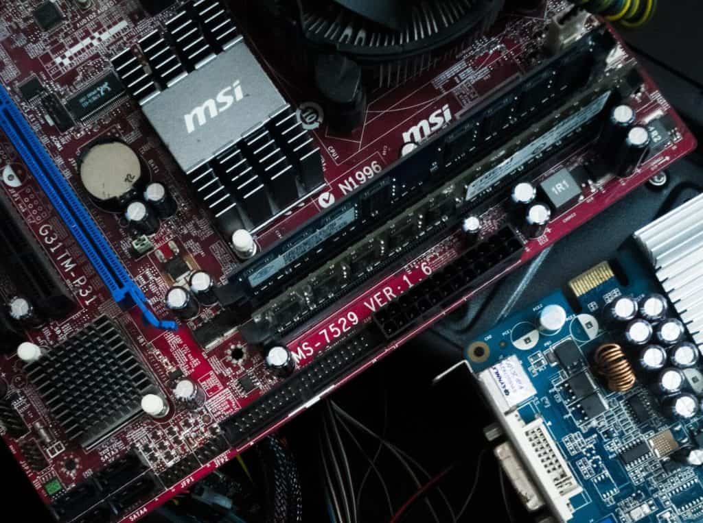 Close-up of a computer motherboard featuring MSI branding, highlighting the intricate electronics. Visible components include RAM slots, capacitors, and connectors on a red circuit board. A graphics card with a fan is partially visible in the foreground, ideal for electronic recycling in Atlanta GA.