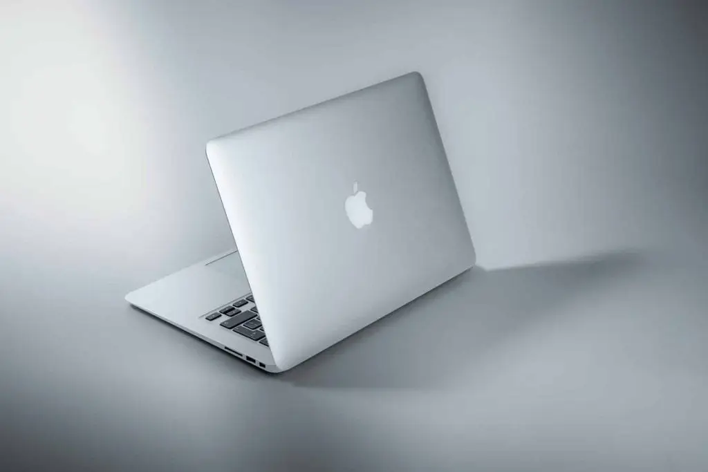 A sleek, silver laptop is partially open, displaying its Apple logo on the back. Set against a minimalist gray background with soft lighting casting a subtle shadow, this elegant piece of technology awaits its next adventure&mdash;or perhaps electronic recycling in Atlanta, GA.