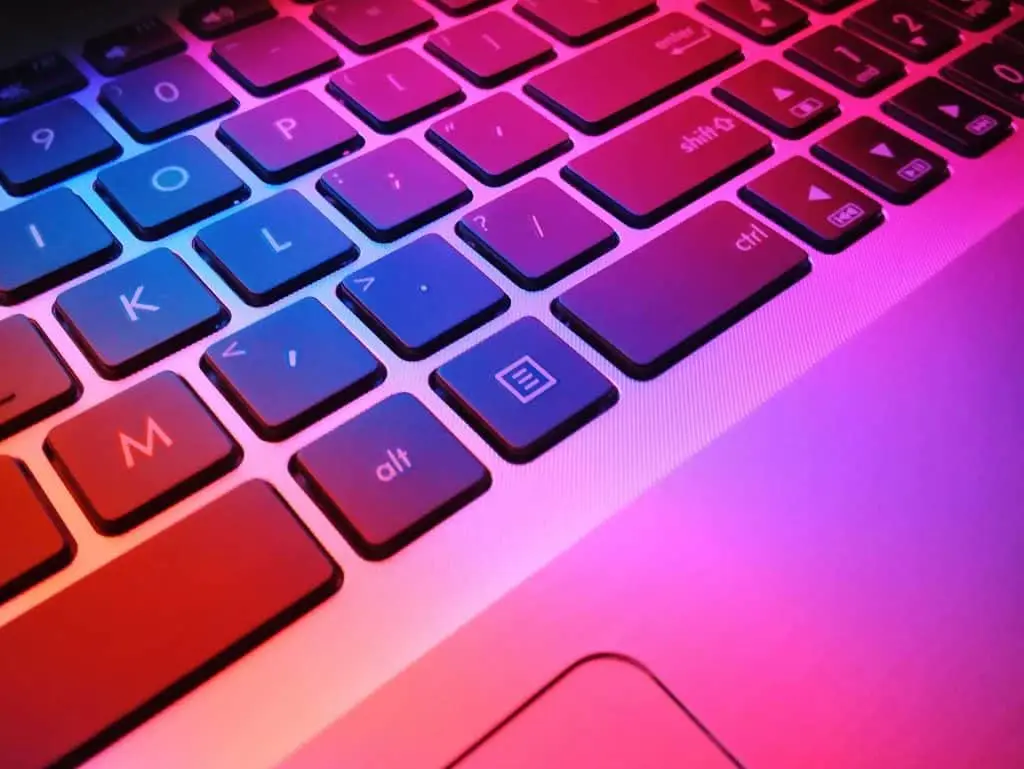 Close-up of a laptop keyboard illuminated with vibrant pink and blue lighting, symbolizing technology and innovation in e-waste management and sustainable IT practices.