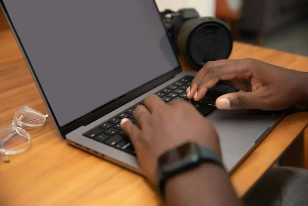 Person typing on a laptop with glasses and camera nearby, illustrating digital engagement in e-waste management discussions.