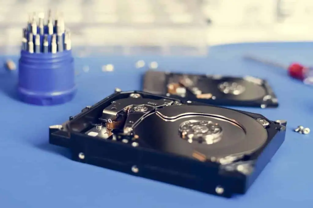 Close-up of open hard drives on a blue surface, hinting at electronics repair. A set of small screwdriver bits in a holder and scattered screws sit nearby, emphasizing a focus on computer hardware repairs, right in the heart of electronics expertise in Atlanta, GA.