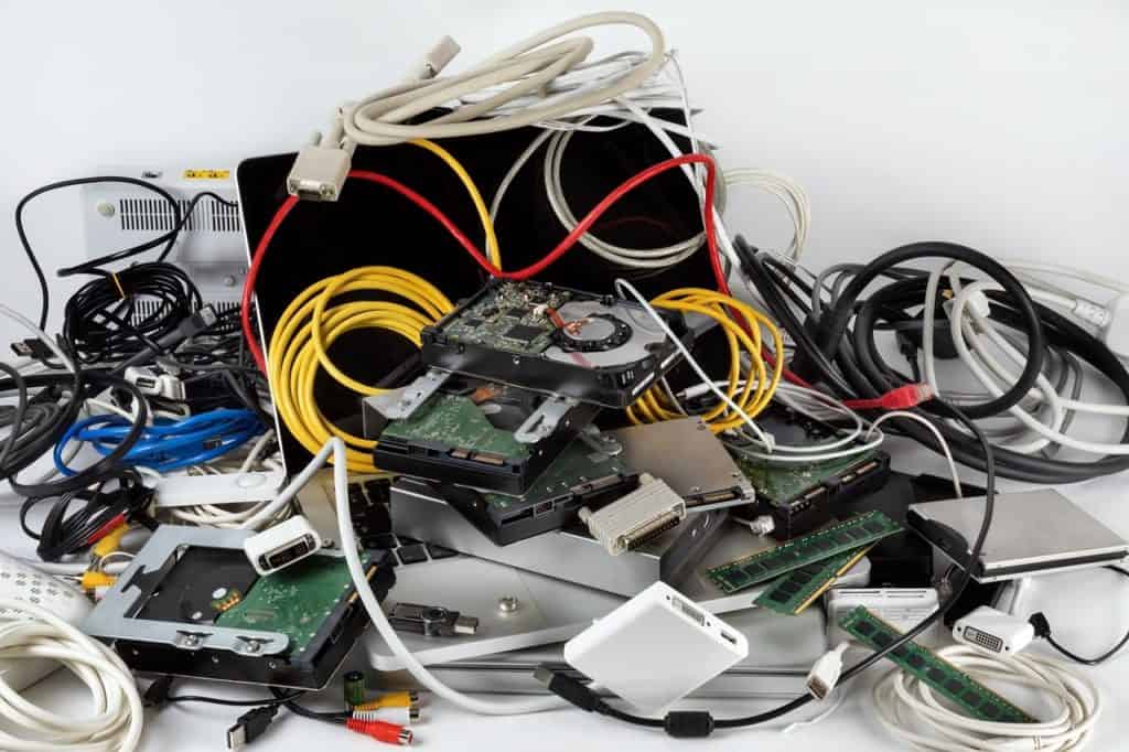 A tangled pile of electronic components, including hard drives, cables, and circuit boards, rests on a white surface in Atlanta, GA. The multicolored cables and haphazardly stacked parts reflect the city's commitment to electronic recycling.