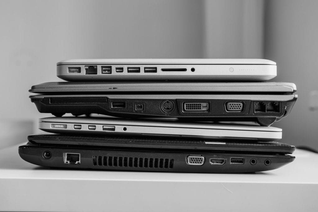 A black and white image of four stacked laptops, each displaying a variety of ports such as USB, Ethernet, and VGA—capturing the essence of electronic recycling in Atlanta GA. The laptops are arranged horizontally on a white surface.