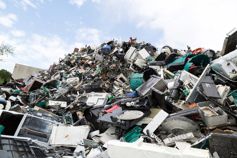 A large pile of e-waste, including old computers, printers, and electronics, awaits recycling under the partly cloudy Atlanta sky. This scene highlights the importance of electronic waste management and encourages using drop-off boxes in Atlanta GA for responsible disposal.