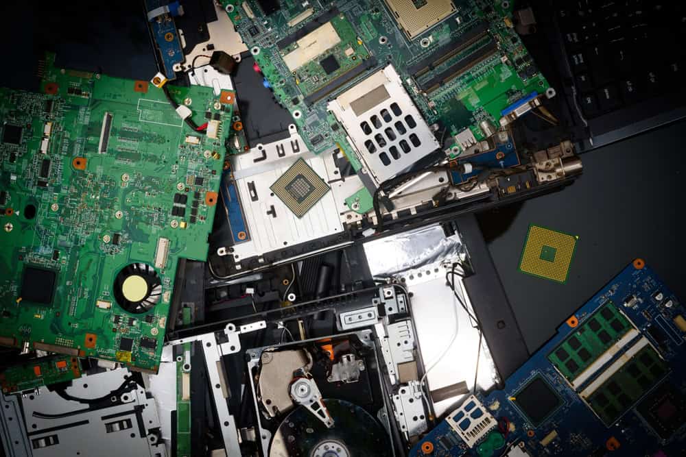 A cluttered pile of computer components, including green circuit boards, a hard drive, RAM modules, and a CPU, sits on a reflective black surface—highlighting the crucial need for responsible electronics waste disposal.