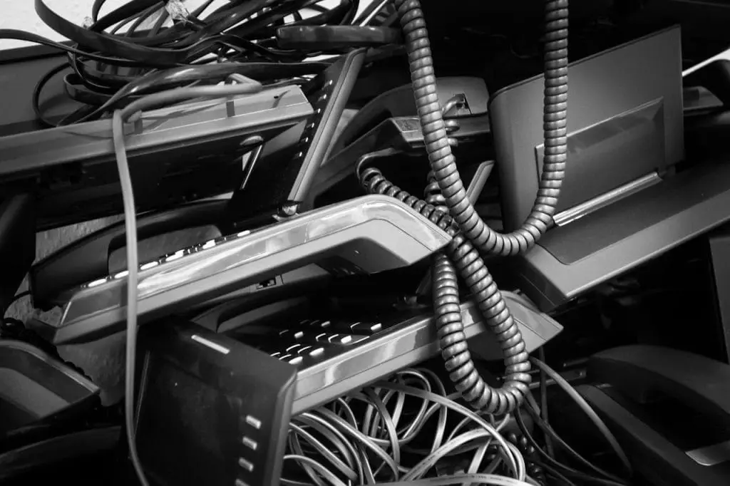 A black and white image of a tangled mess of old telephone handsets, coiled cords, and cables, piled together in a chaotic fashion reminiscent of electronic waste awaiting recycling in Atlanta, GA.