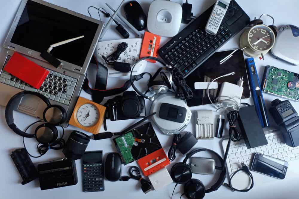 A cluttered collection of various electronic devices and accessories, including laptops, headphones, a keyboard, a clock, a calculator, a mouse, and other gadgets, scattered on a flat surface—perfect for exploring electronics recycling opportunities and learning how to recycle computers wisely.