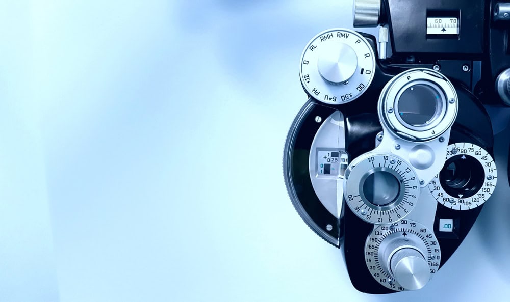 Close-up of an optometrist's phoropter against a light blue background, featuring various dials, lenses, and measurement indicators used for eye examinations. As technology advances, consider electronics recycling to responsibly manage evolving eye care devices.