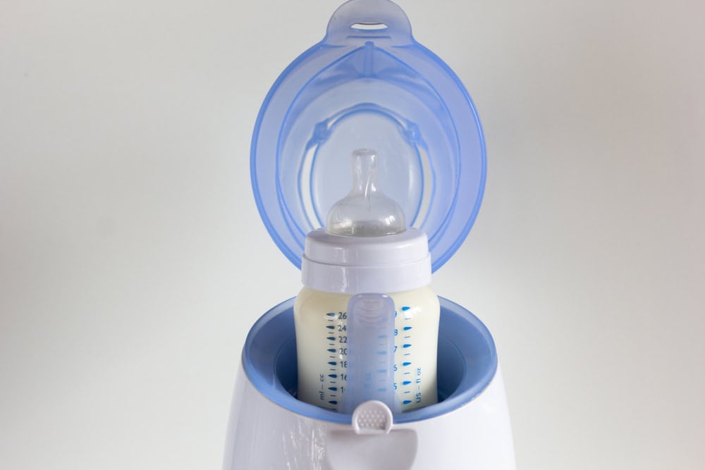 A baby bottle filled with milk rests inside a bottle warmer, its blue lid open and revealing precise measurement markings. By choosing eco-friendly practices like E-waste disposal, we can ensure a healthier planet for the little ones who rely on these warm meals.