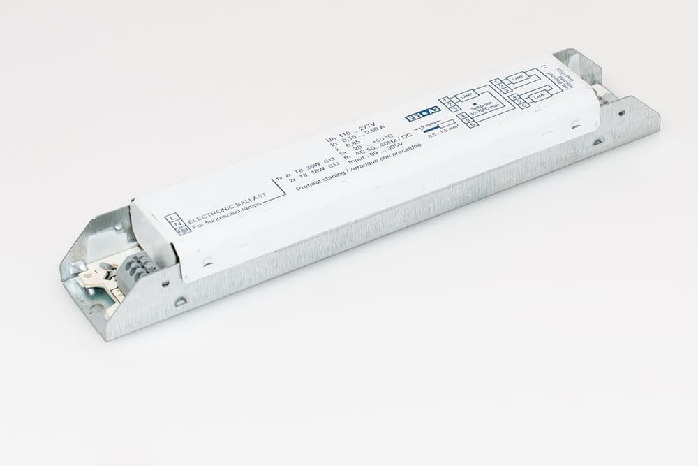 A rectangular electronic ballast with a white casing is designed for ease of electronics recycling. It features printed text and a wiring diagram on top, metal brackets on each end for mounting, and visible electrical connections on one side, all displayed against a plain white background.