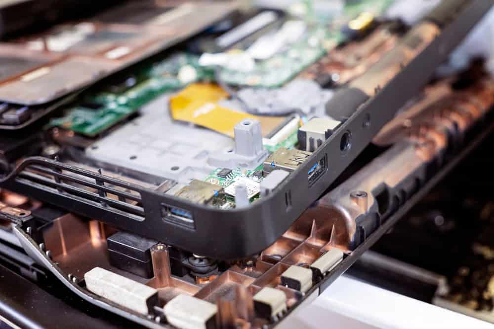 Close-up of a partially disassembled laptop with visible internal components, including circuit boards, ports, and connectors. The device is open, displaying its structure and hardware elements—a vital step in the electronics recycling process.