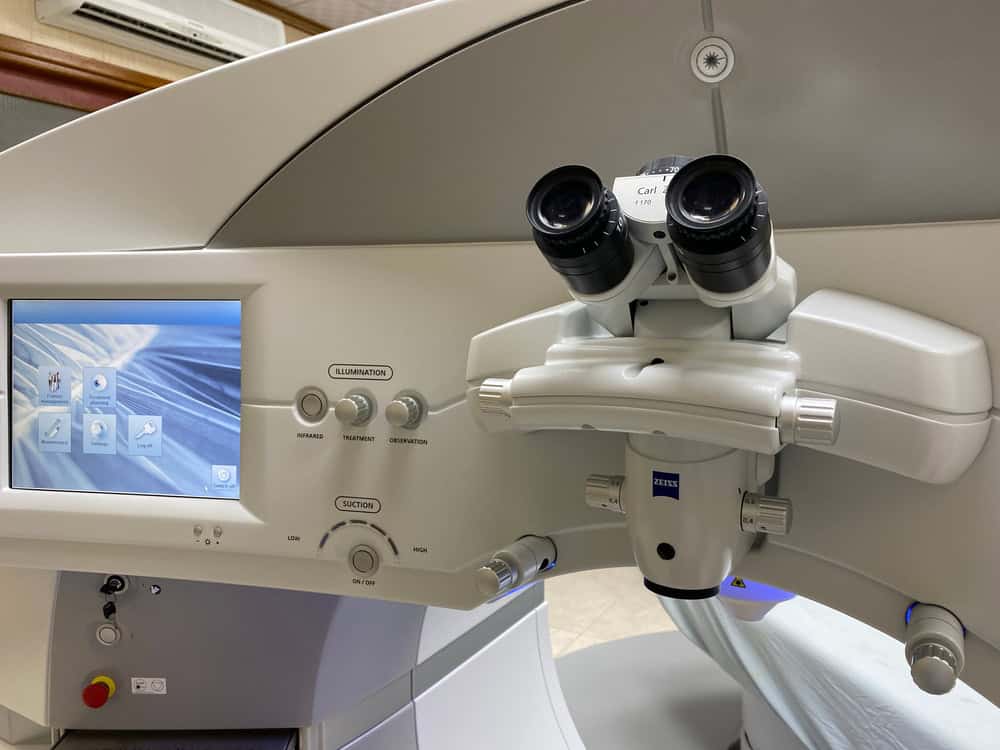 A close-up of a surgical microscope featuring dual eyepieces and a digital display screen, likely used in medical or research settings. The machine, which will eventually require proper electronics waste disposal, has dials and buttons for operation control.