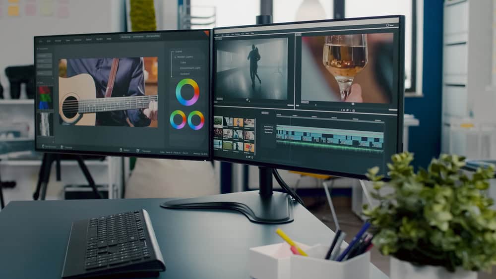 Dual computer monitors on a desk display video editing software. The left screen shows footage of a guitar player and color grading tools, while the right highlights a person with a glass. Amidst the creative setup, remember to recycle computers responsibly to reduce electronics waste disposal.