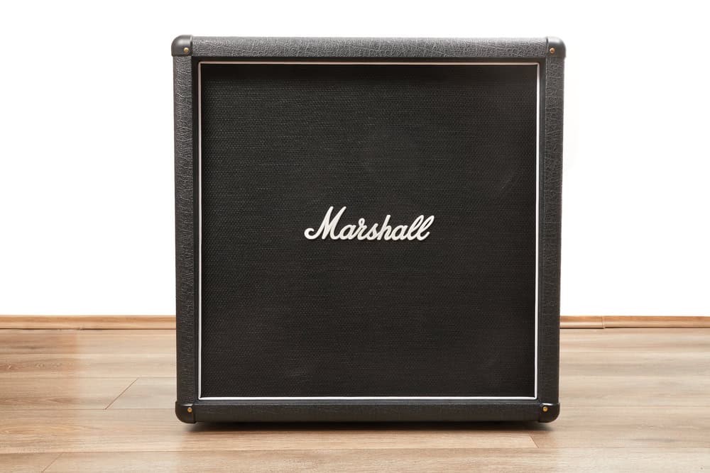 A large black Marshall amplifier cabinet sits majestically on a wooden floor against a plain white wall. Its textured finish and prominent Marshall logo in white stand out, reminding us of the importance of responsible E-waste disposal to ensure electronics like these have a sustainable future.