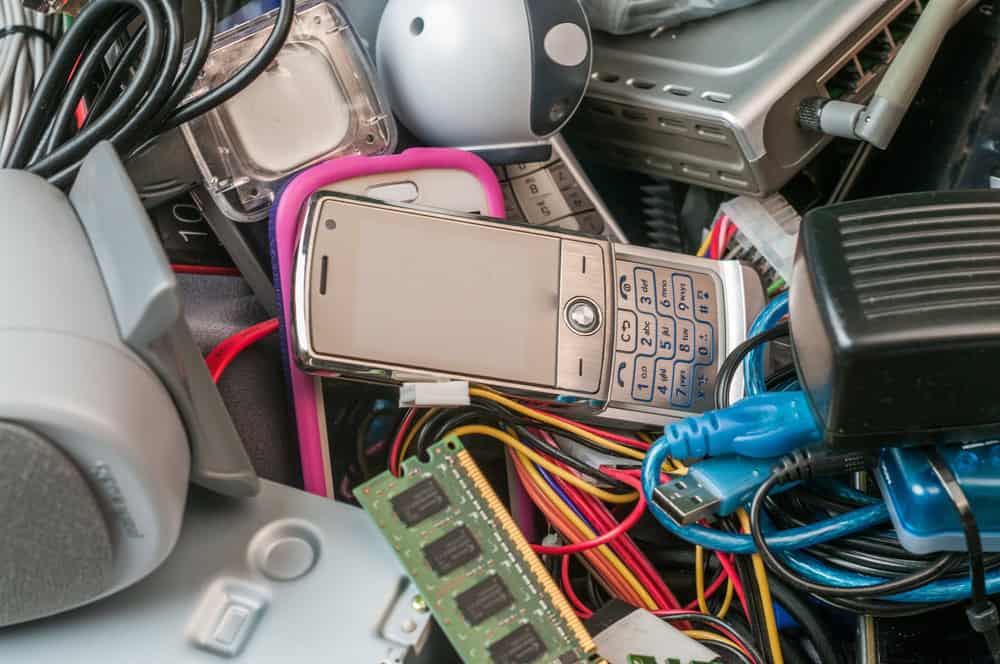 A pile of various electronic waste, including an old cell phone with buttons, tangled wires, computer parts, and small gadgets. The image highlights the importance of electronics recycling in dealing with such outdated technology items.