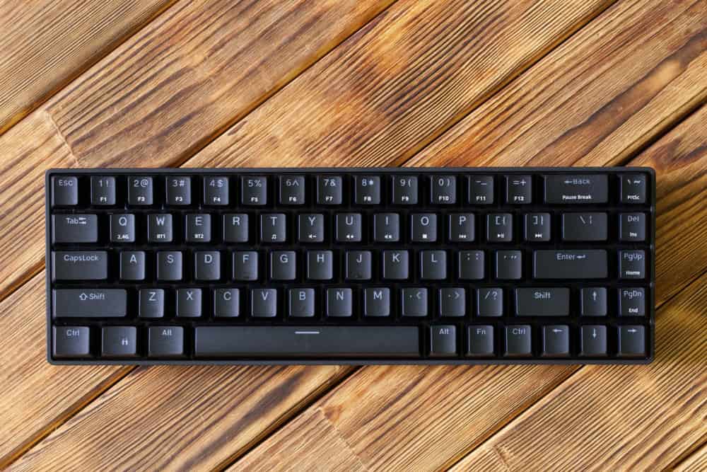 A compact black keyboard rests on a wooden surface, featuring keys with white lettering, perfect for those mindful of E-waste disposal. The keys include standard letters, numbers, and function keys in a condensed layout.