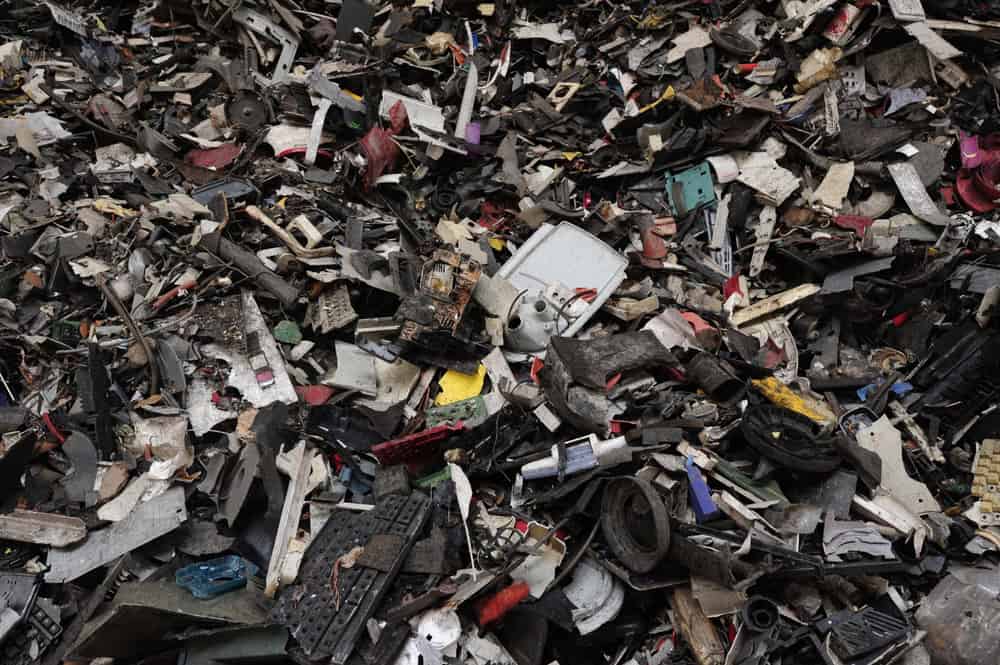 A large pile of assorted electronic waste, including cables, wires, broken devices, and fragments of plastic and metal, forms a chaotic and colorful jumble—highlighting the challenges of effective e-waste disposal.