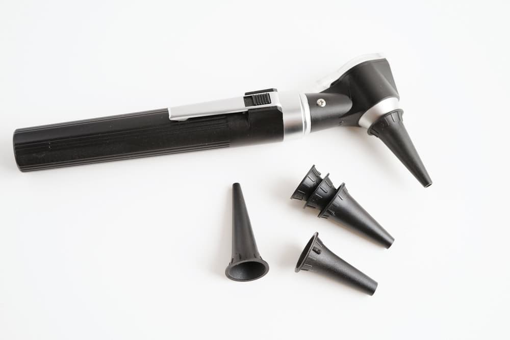 An otoscope with a black handle is shown on a white background. Nearby are four interchangeable specula of varying sizes for ear examinations, highlighting the importance of sustainability in medical tools, much like recycling electronics to reduce waste.