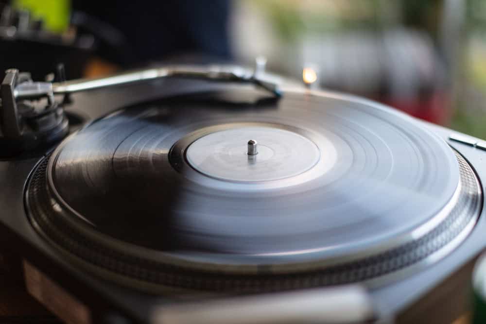 Close-up of a spinning vinyl record on a turntable, a nostalgic nod in our modern world of electronics recycling. The tonearm is slightly blurred and extended toward the record, suggesting music is playing. The background is out of focus, emphasizing the motion and detail of the record.