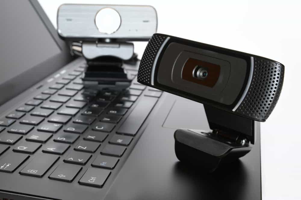 Two black webcams sit on the edge of an open laptop keyboard. One faces the camera while the other faces away, both attached to the laptop's top edge. As electronics recycling becomes more important, consider how to recycle laptops responsibly in a light and neutral environment.