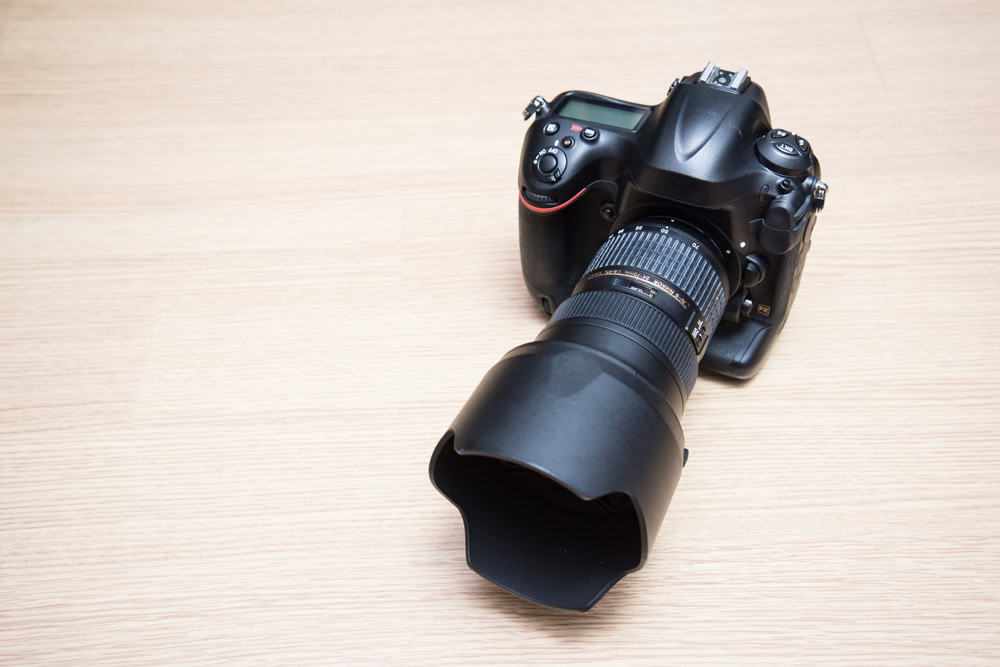 A black DSLR camera with a lens hood rests on a light wooden surface, angled slightly to the left. This piece of technology highlights the importance of electronics recycling, ensuring these valuable devices are disposed of responsibly and sustainably.