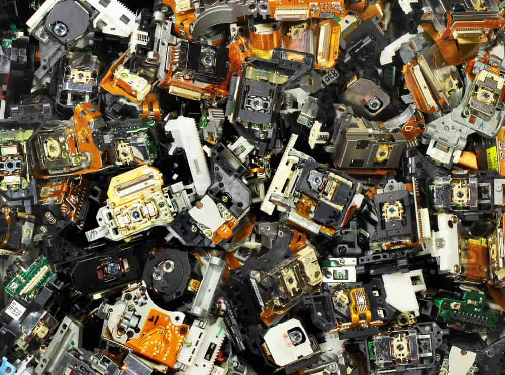 A large pile of dismantled electronic components, primarily orange and black, with various circuit boards, connectors, and metallic parts visible. This densely packed assortment highlights the intricate details often seen in E-waste disposal efforts.