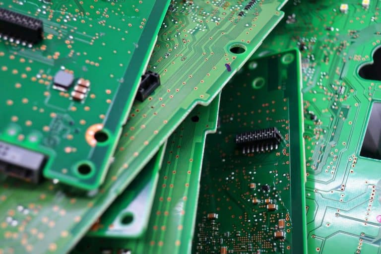 Close-up of overlapping green circuit boards with visible electronic components, copper lines, and connectors. The irregular stack highlights diverse intricate designs and textures, emphasizing the importance of recycling computers to mitigate electronics waste disposal challenges.