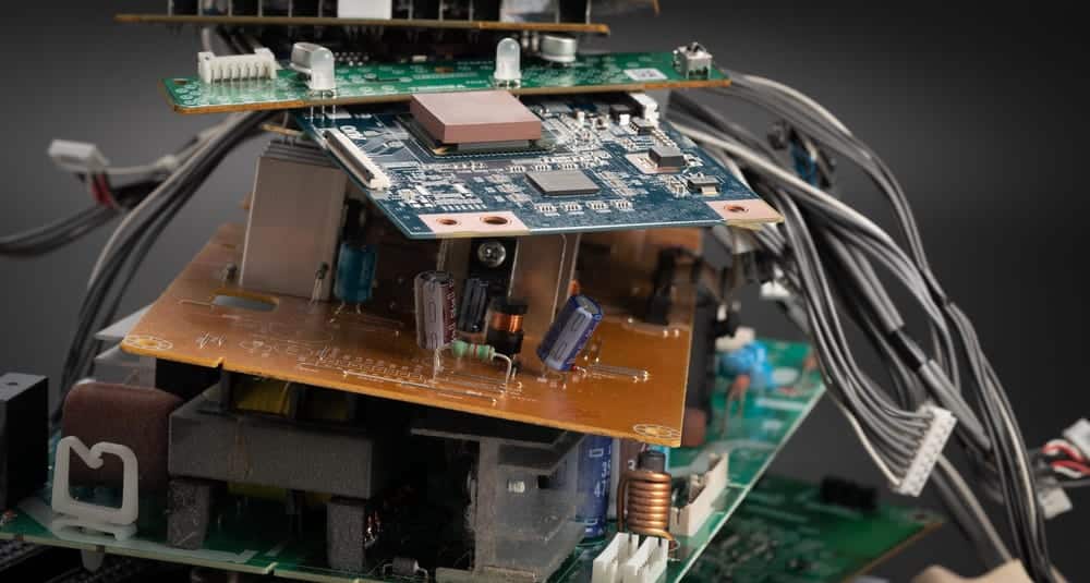 A stack of electronic circuit boards, destined for electronics recycling, is interconnected with various wires. The boards boast multiple microchips, capacitors, and components. The background is blurred, emphasizing the intricate details of the circuitry.