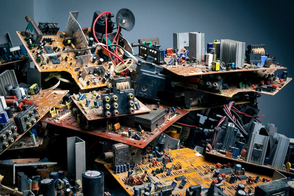 A chaotic pile of assorted electronic circuit boards, resembling the aftermath of electronics waste disposal, features capacitors, resistors, and wires. This complex arrangement sits against a neutral backdrop, highlighting the importance of E-waste disposal to recycle laptops and other devices responsibly.
