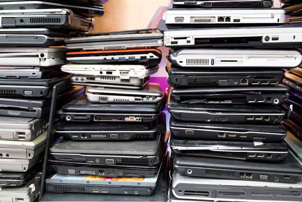 Stacks of various old laptops piled closely together, showcasing a diverse range of models and sizes. The laptops are stacked in two columns, highlighting the importance of electronics recycling and the variety of ports and designs on each device.