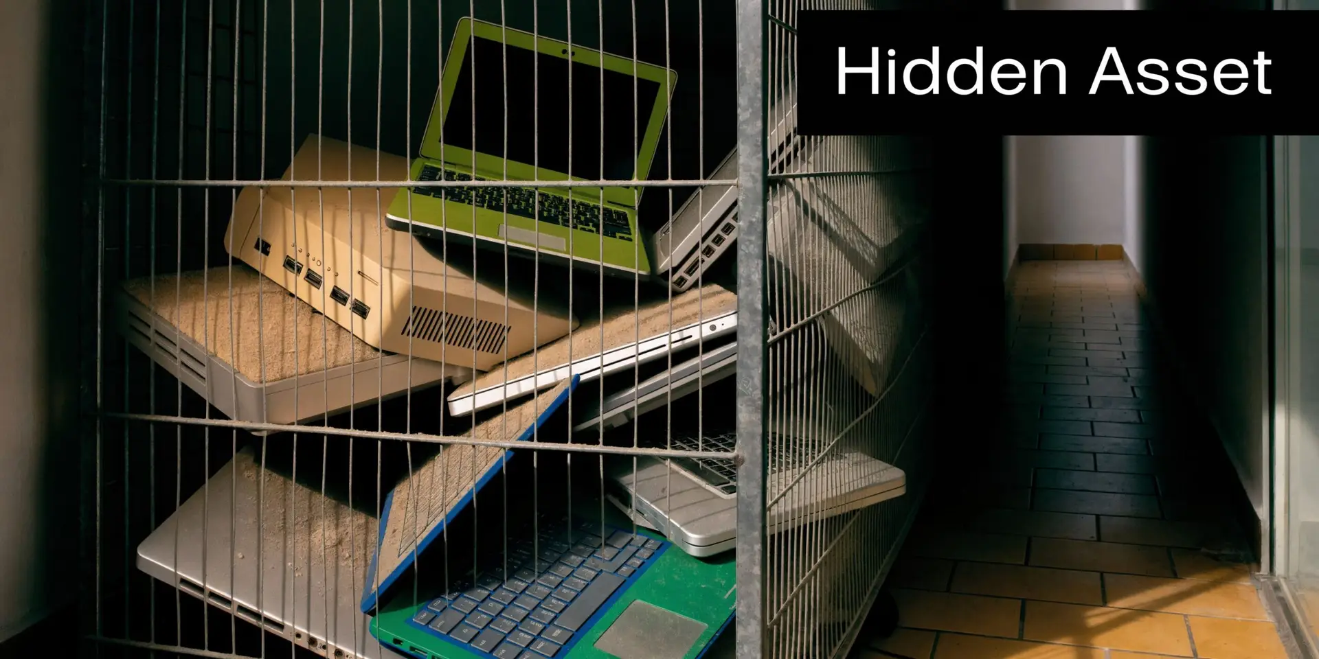 A pile of dusty old laptops and computer equipment stored inside a metal storage cage in a hallway.