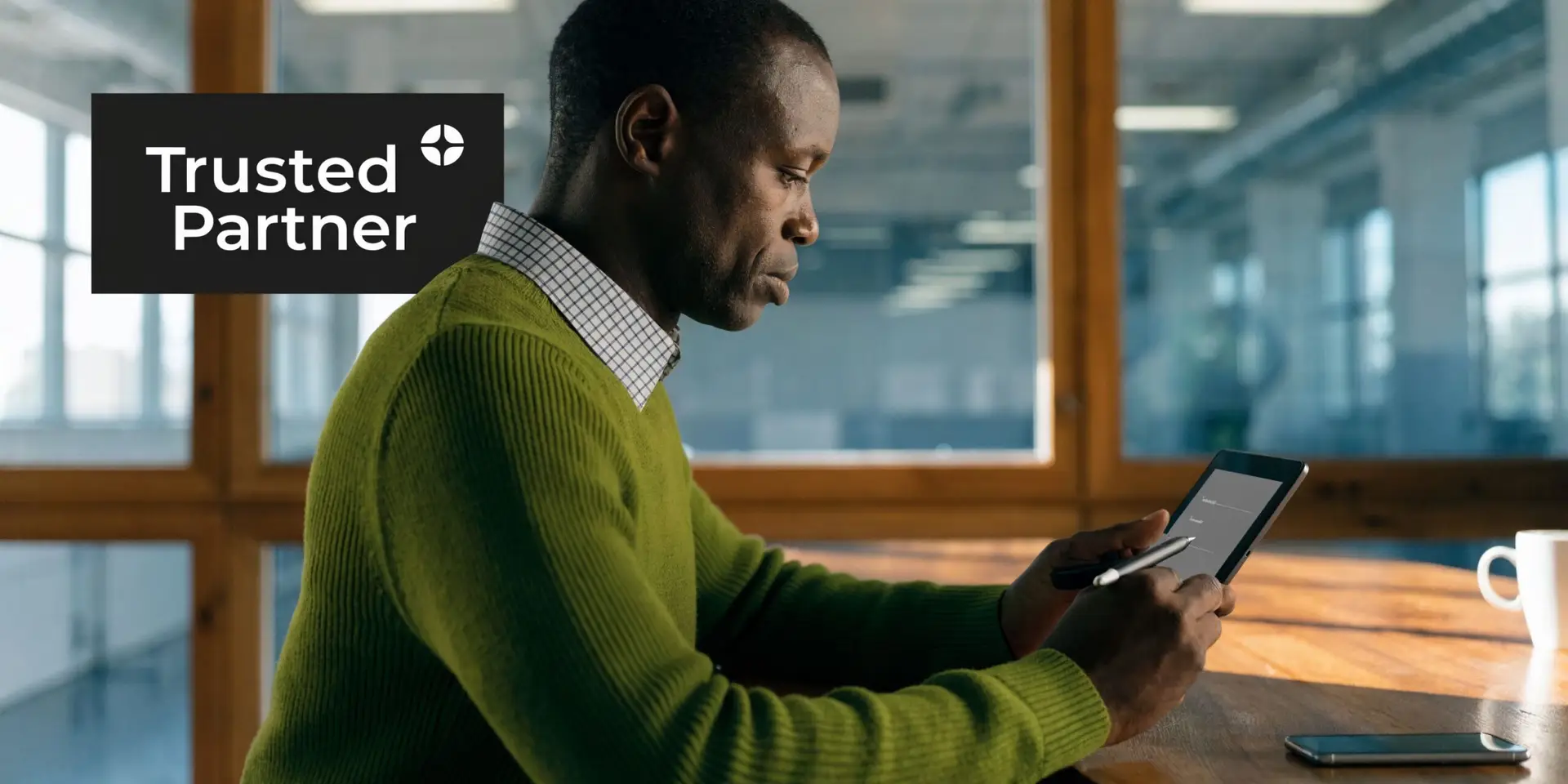 A professional man in a green sweater using a digital stylus on a tablet at his desk.