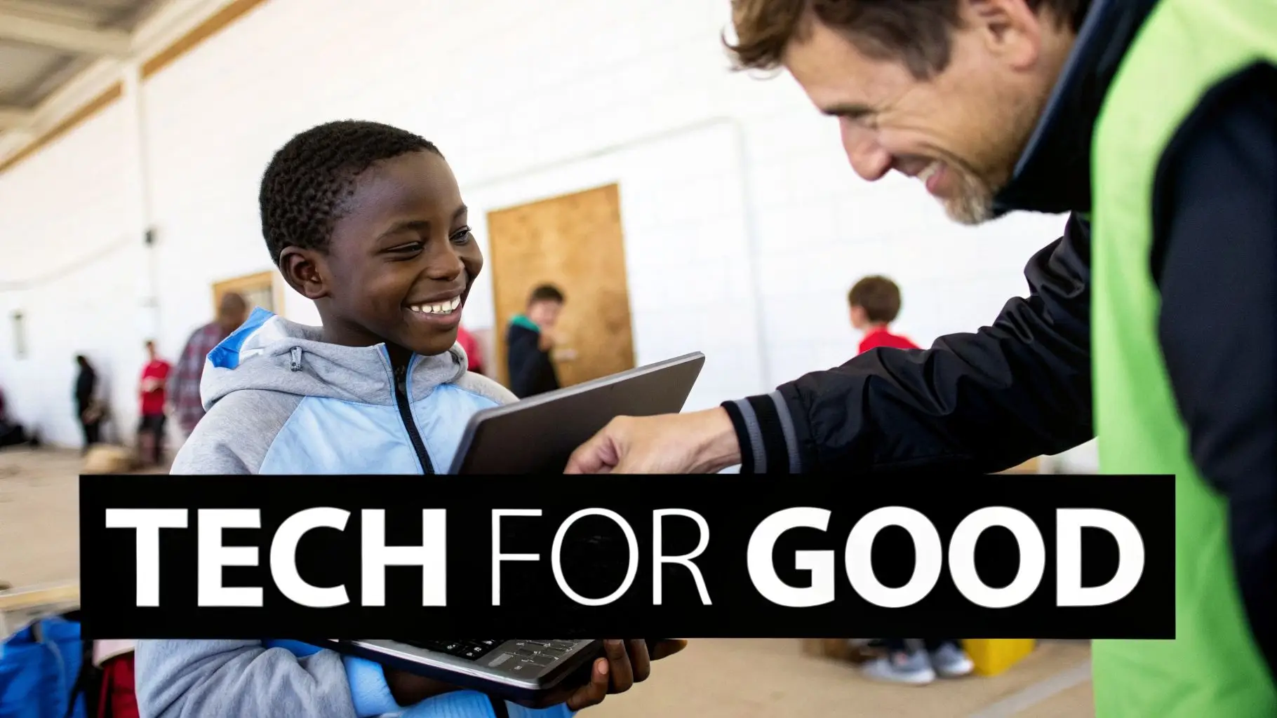 A happy young boy receives a laptop from a smiling man at a 'TECH FOR GOOD' event.