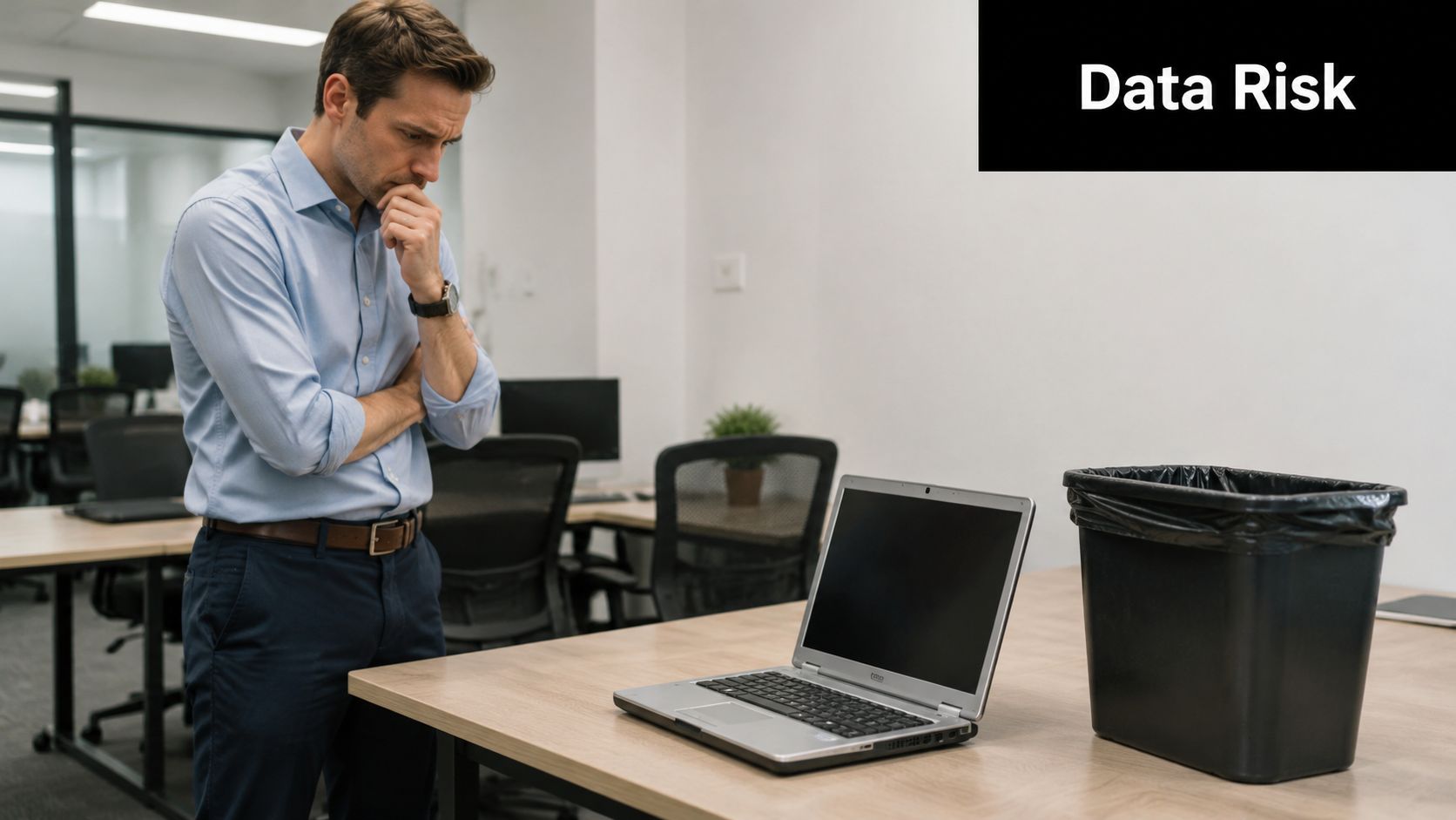 A concerned professional standing in an office contemplating whether to discard his laptop in the trash bin.