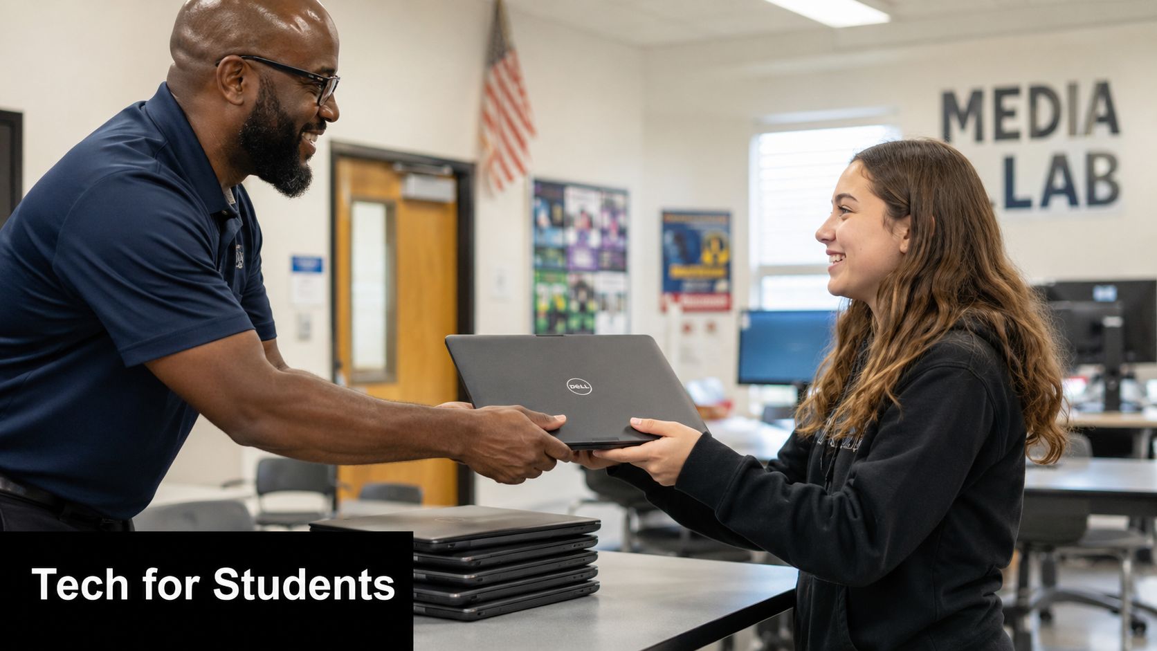 A teacher handing a laptop to a smiling student in a school media lab setting.