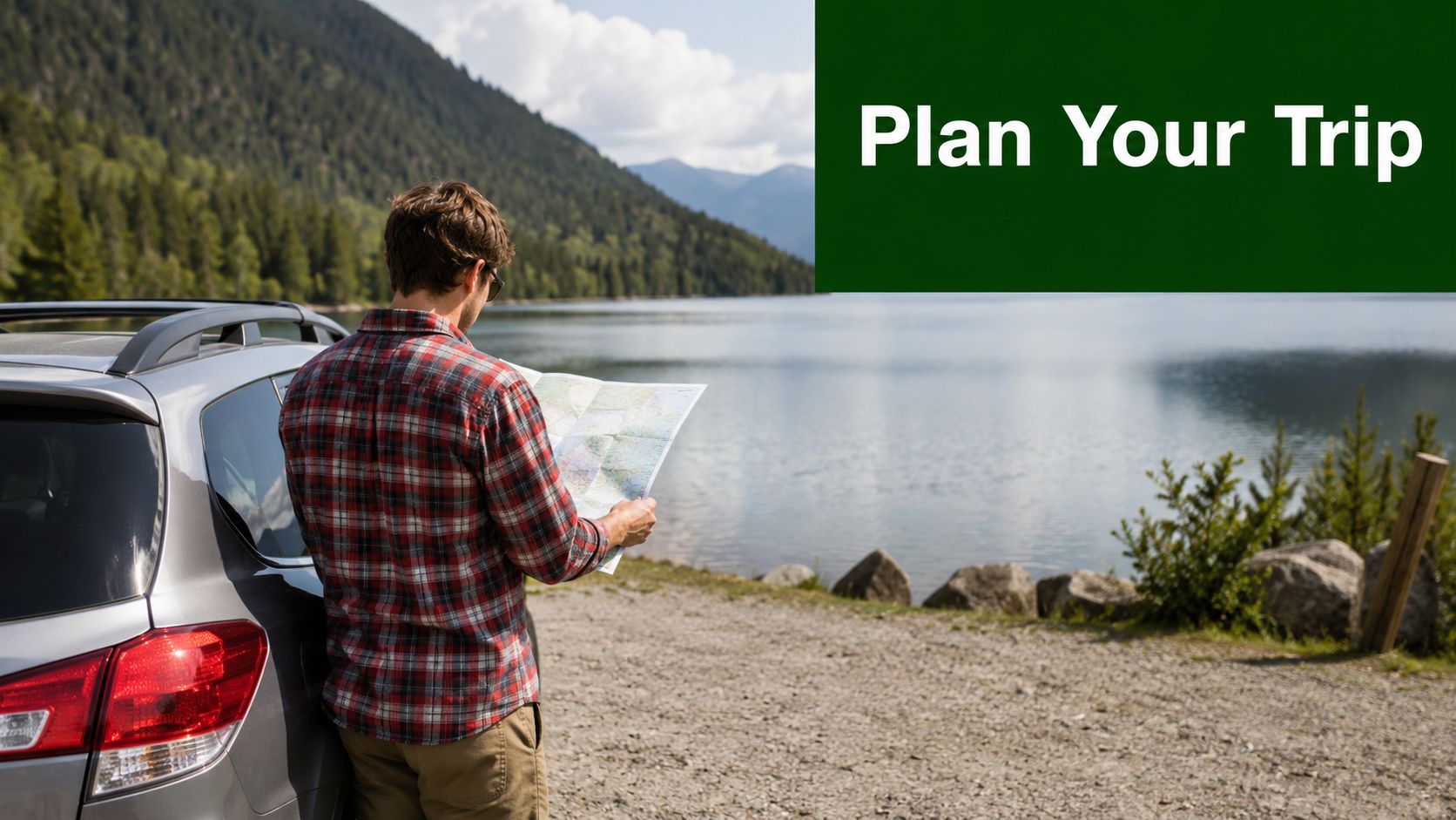 A man in a plaid shirt stands by his car looking at a map near a lake.