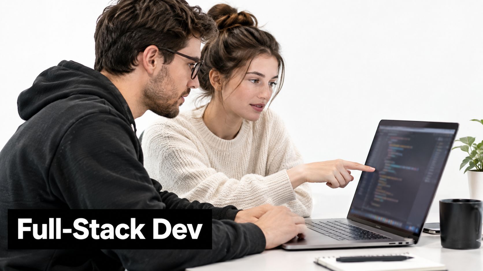 A male and female developer collaborating on code on a laptop in a bright office environment.