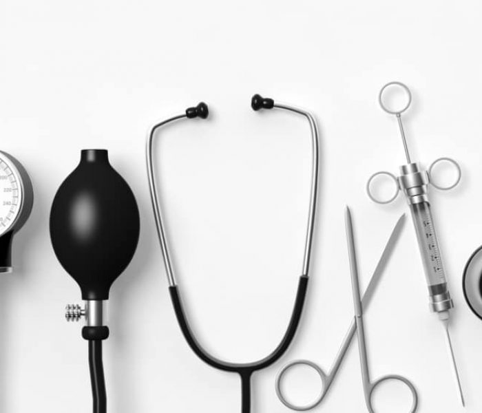 Medical equipment on a white background, featuring a sphygmomanometer, stethoscope, syringe, scissors, forceps, and otoscope arranged neatly in a row—much like how we should approach electronics waste disposal: organized and mindful of proper E-waste disposal practices.